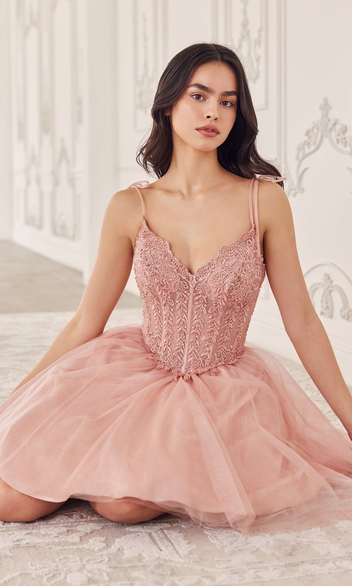 A woman in the Ladivine Embroidered Lace Homecoming Dress CD0236 with blush pink tulle sits on a patterned rug in an elegant, white ornate room.